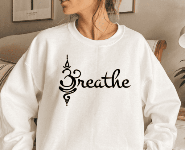 woman wearing a white sweatshirt with the word "Breathe" on the front in black. The "B" in Breathe is the symbol for Namaste instead of an actual letter B.