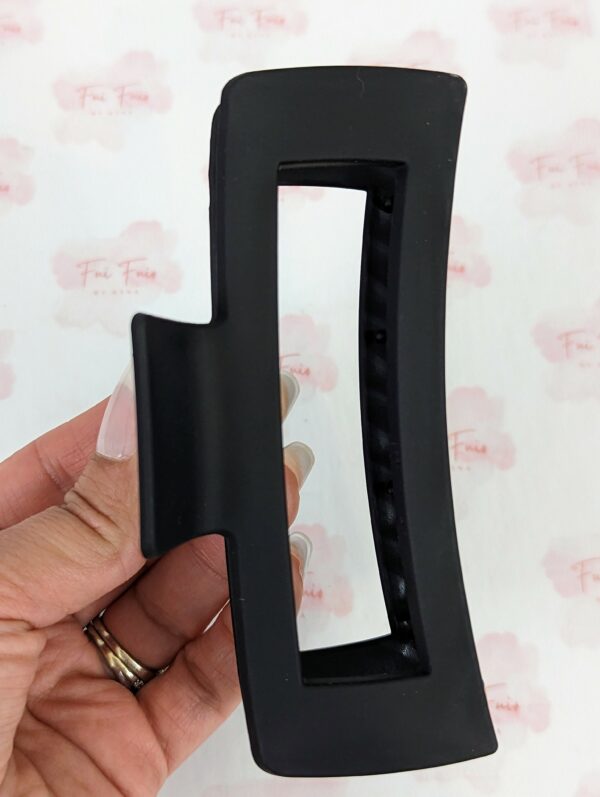 XL black hair clip held by a woman's hand. it has a hollow center against branded paper.