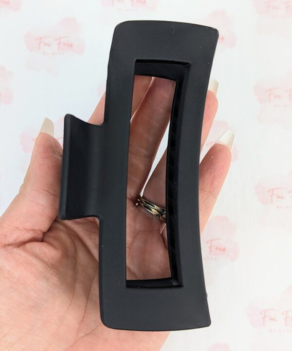 Black XL hair claw clip with hollow center held in womans palm to show size of hair claw measurements.
