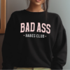 Woman with brown hair wearing a black crewneck sweatshirt with the phrase "Bad Ass Babes Club" written in Pink and White