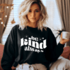 woman wearing black crewneck sweatshirt with the phrase "be kind always" written in the color black in a warped text.