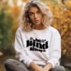 woman wearing a white sweatshirt with the phrase "be kind always" written in a warped text in black color.