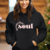 Woman wearing black hoodie with the phrase "Beautiful Soul" written in pink on the front. The word beautiful is curved around the front part of the word "soul".