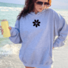 woman wearing a gray hoodie with a daisy that has a smiling face centered on her chest.