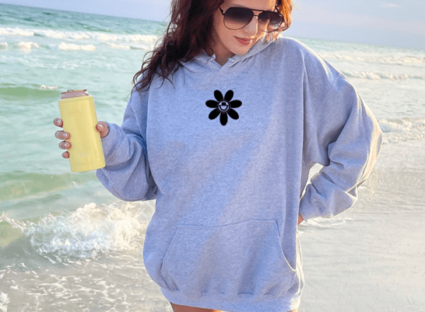 woman wearing a gray hoodie with a daisy that has a smiling face centered on her chest.