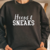 Woman wearing a black crewneck sweatshit with the phrase "Hoops and Sneaks" written in white across the chest.