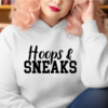 Woman wearing a white hoodie with the phrase "Hoops and Sneaks" written across the chest in black.