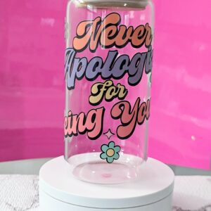 Transparent glass can with bamboo lid with the phrase "Never Apologize for Being You" written in colorful letters. Colorful nostalgic daisy decorations on the sides.