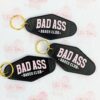 Three black motel keychains with a gold jump ring and key ring. The phrase "Bad Ass Babes Club" written in light pink and white.