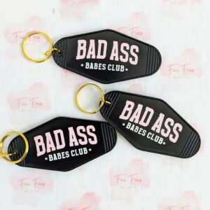 Three black motel keychains with a gold jump ring and key ring. The phrase "Bad Ass Babes Club" written in light pink and white.