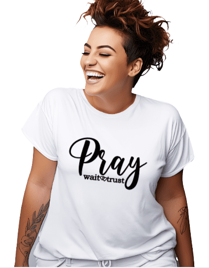 Woman wearing a white t-shirt with the phrase "Pray Wait Trust" written across the chest in black cursive lettering.