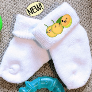 White baby socks with the image of 3 quenepa buddies on the side.