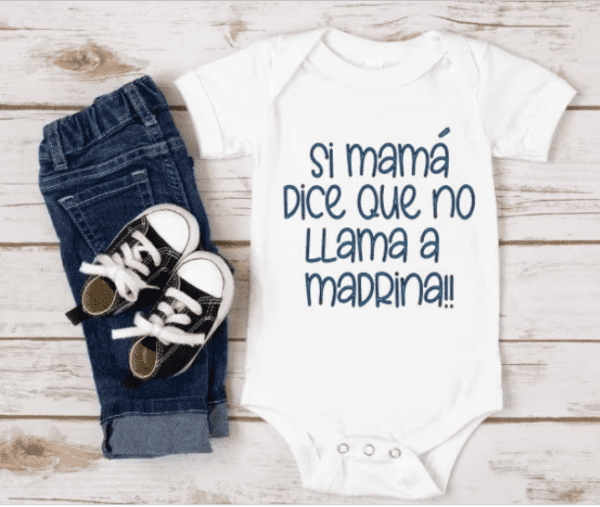 white one piecee baby bodysuit with the phrase "si mama dice que no llama a madrina" printed in blue on the front.