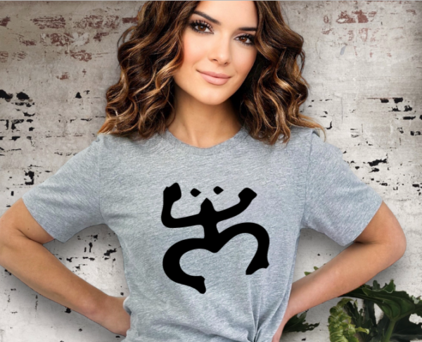 Woman wearing a gray t-shirt with a Taino Coqui on the chest in black.