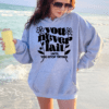 Woman on the beach wearing a gray hoodie with the phrase "You never fail until you stop trying" holding an insulated tumbler.