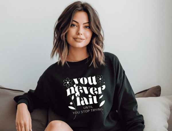 woman wearing a black crewneck with the phrase "You never fail until you stop trying" written in warped text.
