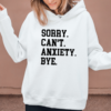 woman wearing a white hoodie with the phrase "Sorry. Can't. Anxiety. Bye" in a collegiant font.
