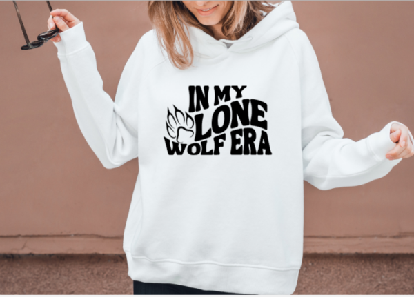 woman wearing a white hoodie with the phrase "In my lone wolf era" written in a retro wavy font and a wolf paw print next to the word "lone"