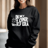 woman wearing a black crewneck sweatshirt with the phrase "in my lone wolf era" written in a retro wavy font with a wolf paw print next to the word "lone"