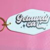 White motel keychain with gold keying. Phrase "Getaway Car" written in pink with black shadow. Retro font.