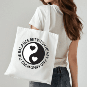 Woman with white tote bag on her shoulder. The bag has the yin and yang symbol with hearts where the circles normally are. The quote circling the yin and yang reads, "Find the balance between heart and mind"
