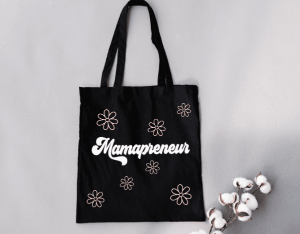 Black tote bag with the word "Mamapreneur" on the front with pink daisy flowers around it.