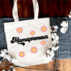 white tote bag with the word "mamapreneur" written on the front in a retro font. Individual daisy like flowers are above and below the word.