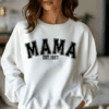 woman wearing a white crewneck sweatshirt with the phrase MAMA and EST. 1997. This shirt can be customized with the year of choice