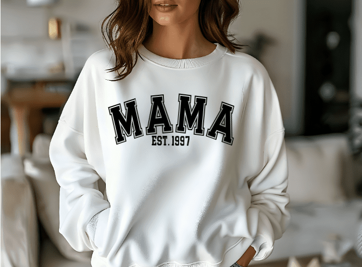 woman wearing a white crewneck sweatshirt with the phrase MAMA and EST. 1997. This shirt can be customized with the year of choice