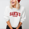 Woman wearing a white crewneck sweatshirt with the phrase "Santa's Favorite" written in red collegiate font.