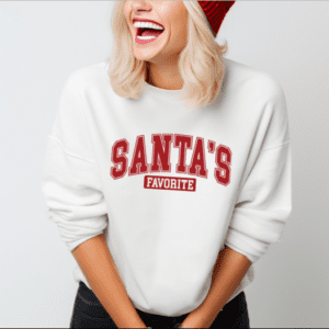 Woman wearing a white crewneck sweatshirt with the phrase "Santa's Favorite" written in red collegiate font.