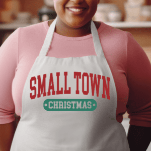 Woman wearing a white apron with the phrase Small Town in red and Christmas underneath in green.