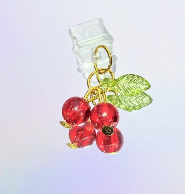 summer phone charm. two small resin cherries with one small green leaf held together with gold wires and connected to a clear silicone usb-c dust plug