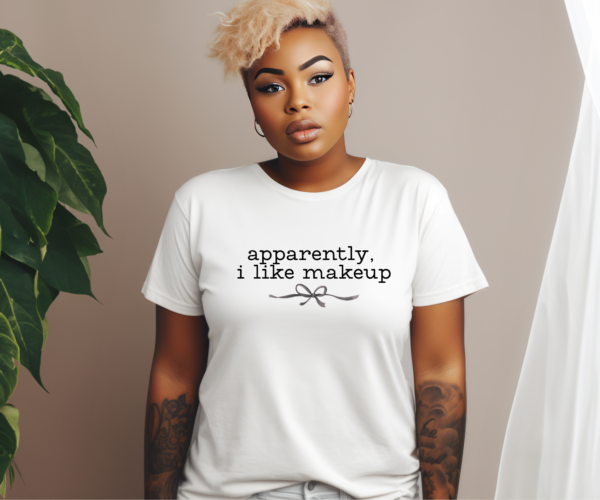 Woman wearing white t-shirt that reads "apparently I like makeup" with a delicate bow underneath. Black lettering.