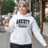 Woman walking on the sidewalk by a storefront holding a coffee cup. The hoodie reads "Anxiety University Honors Program"