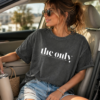 Person wearing a dark gray oversized T‑shirt that reads “the only person I had to convince was me,” sitting in a car holding a tumbler.