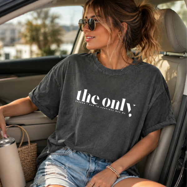 Person wearing a dark gray oversized T‑shirt that reads “the only person I had to convince was me,” sitting in a car holding a tumbler.